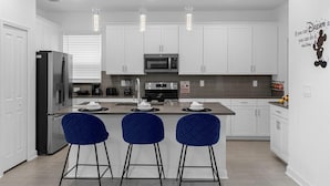 A modern kitchen with white cabinets, stainless steel appliances, and blue bar stools.