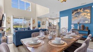 A modern dining area with a wooden table set for six, a blue sofa in the background, and a large abstract painting on the wall.