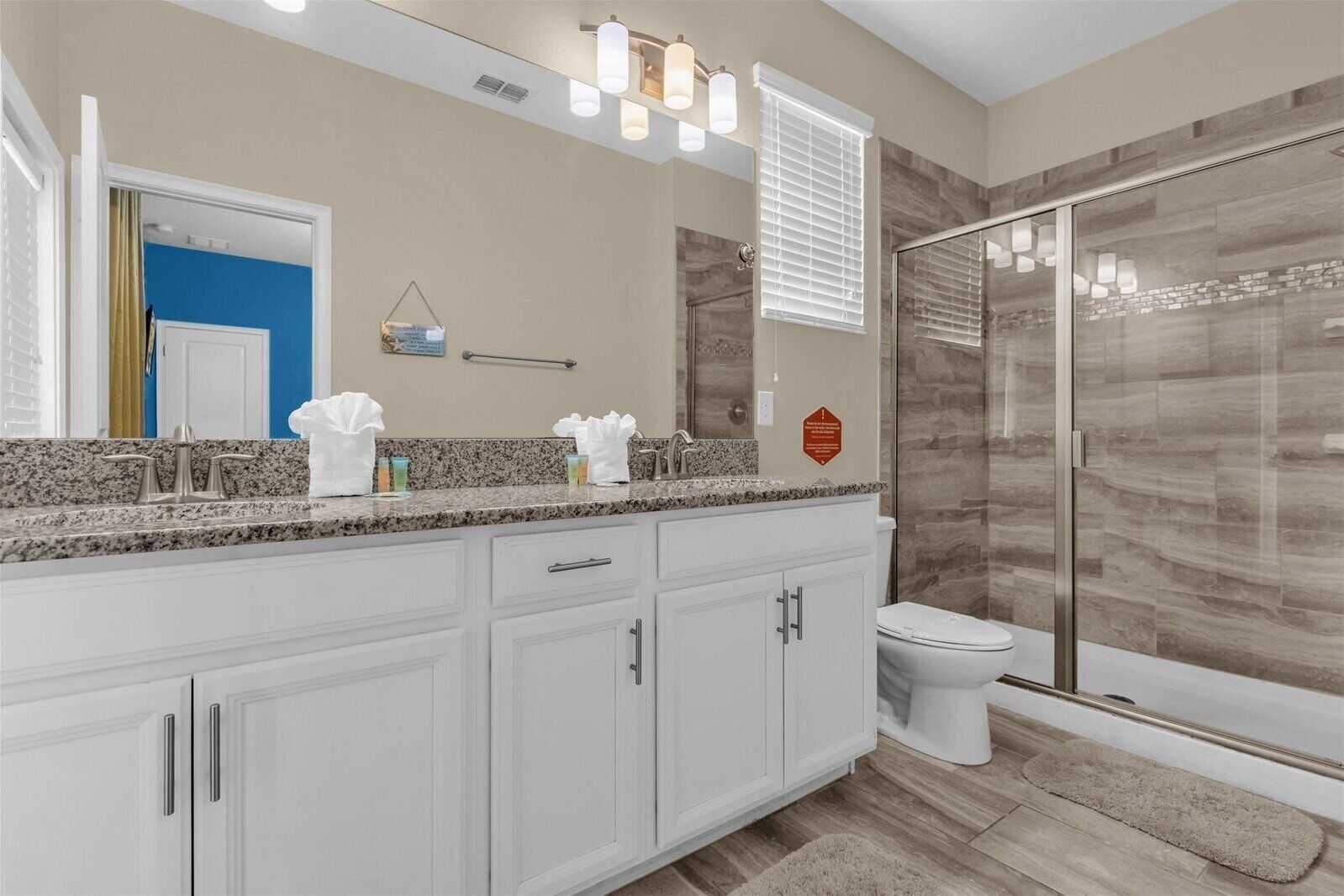 A modern bathroom with a granite countertop, white cabinetry, a glass shower enclosure, and a toilet.