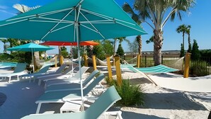 A beachside lounge area with sun loungers and umbrellas, a sandy beach, and palm trees. - Magnificent 5BR Home at Windsor Island Resort (Davenport)