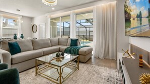 A modern living room with a beige sectional sofa, a glass coffee table, and a view of a natural landscape through large windows. - Magnificent 5BR Home at Windsor Island Resort (Davenport)