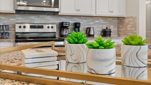 A kitchen with white cabinets, a stainless steel oven, and a marble countertop. There are three green plants in marble pots on the counter. - Magnificent 5BR Home at Windsor Island Resort (Davenport)