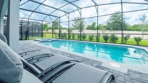 Una piscina exterior cubierta con sillones de descanso, rodeada por un cerramiento de cristal y vistas a un paisaje verde.