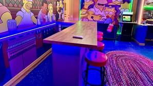 Zona de bar con un mural temático de Los Simpson, taburetes y una barra de madera.