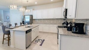 Una cocina moderna con armarios blancos, encimera de granito, lavavajillas integrado y cafetera.