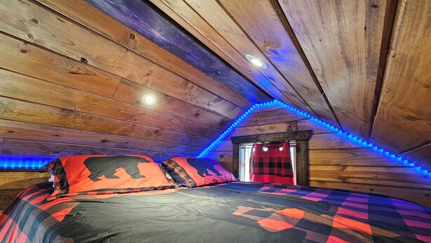 Un dormitorio acogedor en el ático, con techo de madera, cama con ropa de cama estampada y luces LED azules a lo largo del techo.