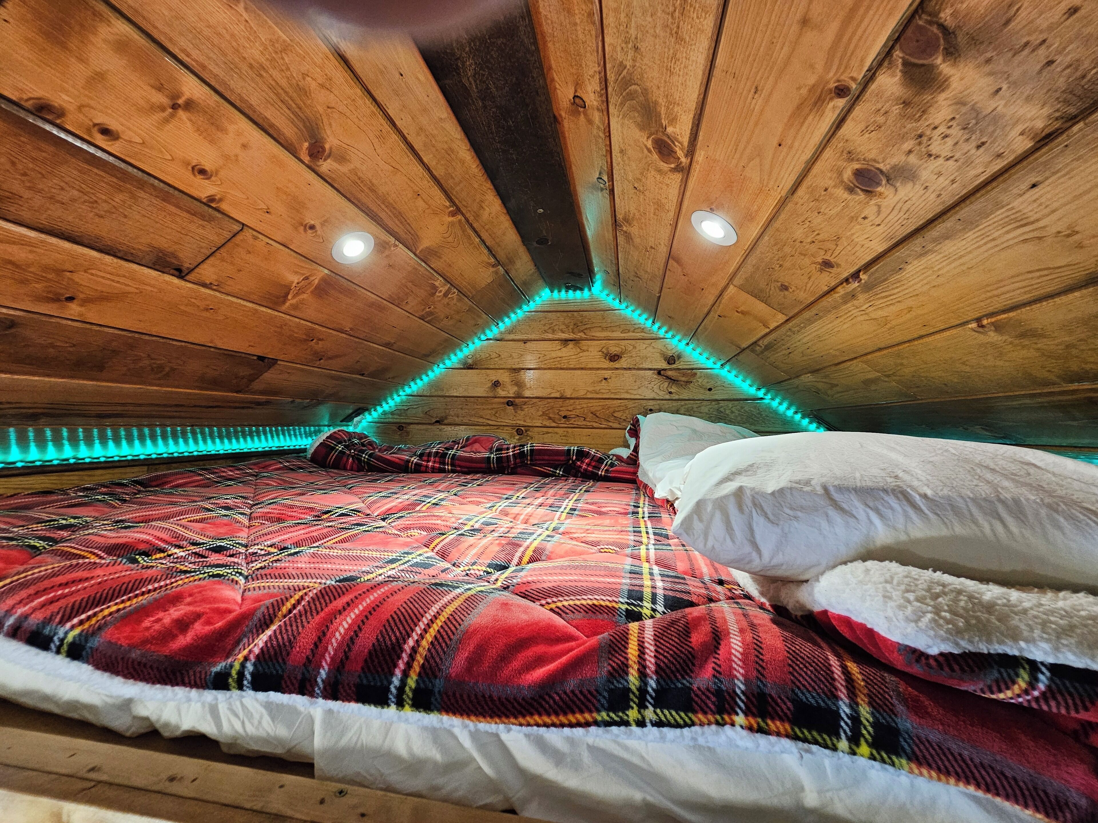 A cozy attic bedroom with a wooden ceiling, a plaid bedspread, and a white pillow.