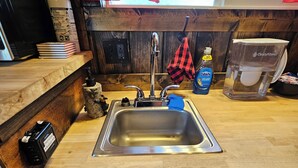 Una cocina con un lavamanos de acero inoxidable, encimera de madera y una ventana con cortina roja.