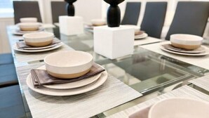 A dining table set with plates, bowls, and napkins, with chairs and a decorative black object in the background.