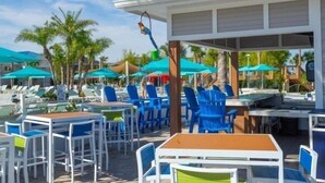 An outdoor seating area with tables and chairs, umbrellas, and a pool in the background.