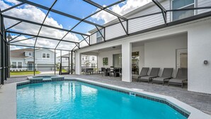 Una piscina con un porche cubierto, sillas de descanso y vistas a casas vecinas.