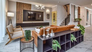 Ein modernes Wohnzimmer mit Sofa, Fernseher, Lampe und einer Treppe.
