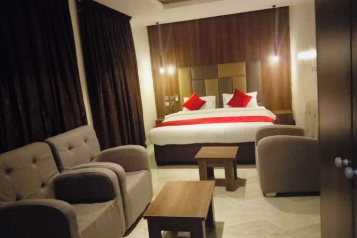 Una habitación de hotel con una cama grande, dos sillones, una mesita y un cabecero de madera.