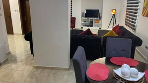 Een moderne woonkamer met een zithoek, een eettafel met plaatsmatten, en een televisie op de achtergrond.