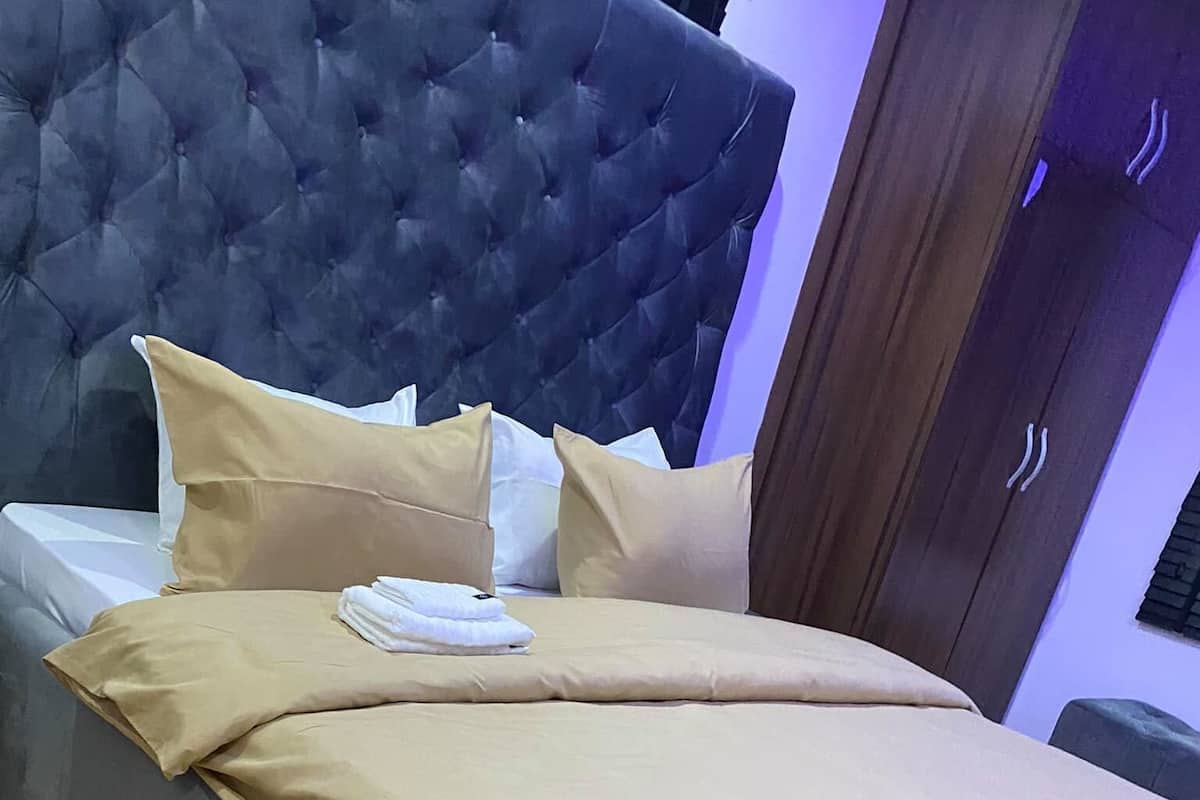 Una cama con cabecera capitonada, ropa de cama color beige y una alfombra morada.