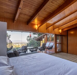 A bedroom with a large bed, a balcony with chairs, and a view of the outdoors. - Beautiful Country House Pool & Views (Cuernavaca)