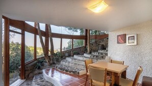 A dining area with a stone staircase leading to a balcony, wooden beams, and a view of the surrounding landscape.
