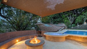 An outdoor patio area with a fire pit, a pool, and a covered seating area.