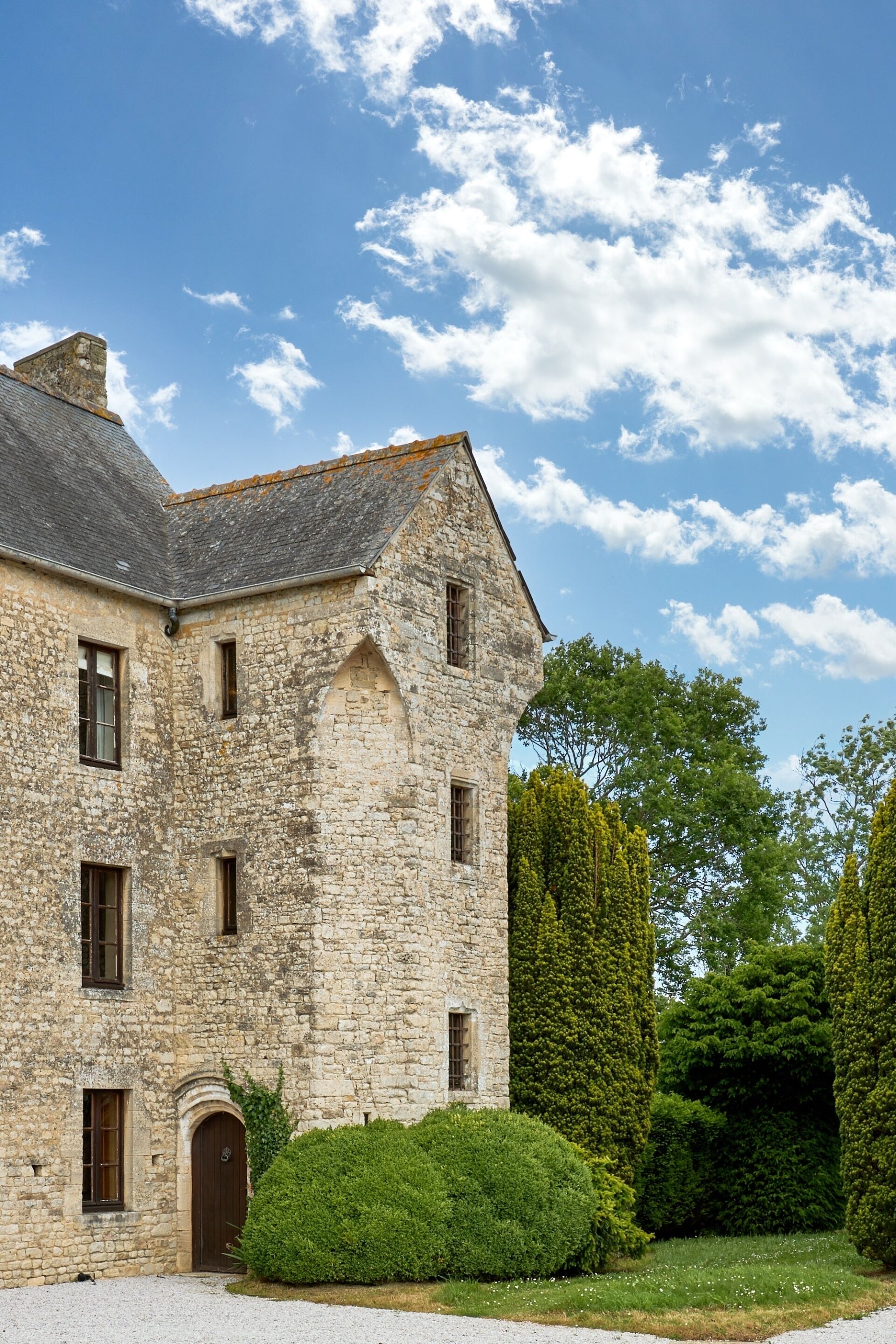 Un bâtiment en pierre doté de nombreuses fenêtres et d’une porte, entouré d’un espace verdoyant bien entretenu et d’arbres.