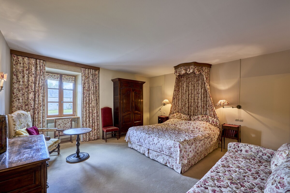 Ein Schlafzimmer mit einem großen Bett, einem roten Sessel, einem kleinen Tisch und einem Kleiderschrank.