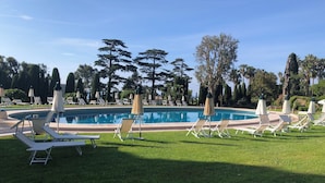 A pool area with lounge chairs and umbrellas, surrounded by trees and a clear sky.