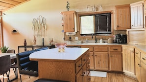 A kitchen with wooden cabinets, a white countertop, and a dining area with a table and chairs. - Superhome Riverbottoms Home in Bismarck (Bismarck)