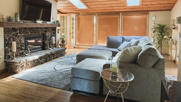 A cozy living room with a stone fireplace, a large sectional sofa, and a ceiling fan. - Superhome Riverbottoms Home in Bismarck (Bismarck)