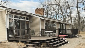 A single-story house with a covered patio area, a brick chimney, and a deck with steps leading to a table and chairs. - Superhome Riverbottoms Home in Bismarck (Bismarck)
