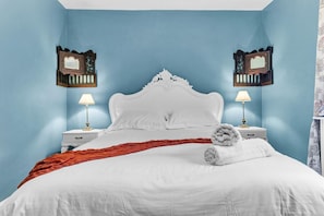 A bedroom with a white bed, two nightstands with lamps, and two wall-mounted mirrors.