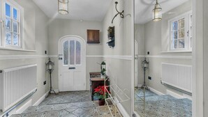 Um corredor com piso estampado, uma porta branca com painel de vidro jateado e luminárias fixadas na parede.