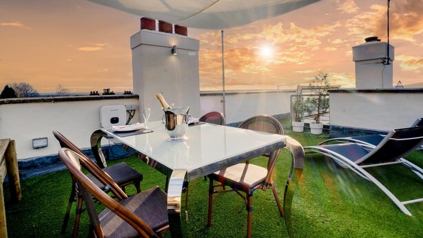 Terraço no telhado com mesa de vidro, cadeiras e vista para o pôr do sol.