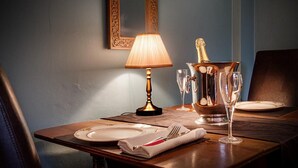 Uma mesa de jantar posta com pratos, talheres, uma lâmpada, uma garrafa de champanhe e copos.