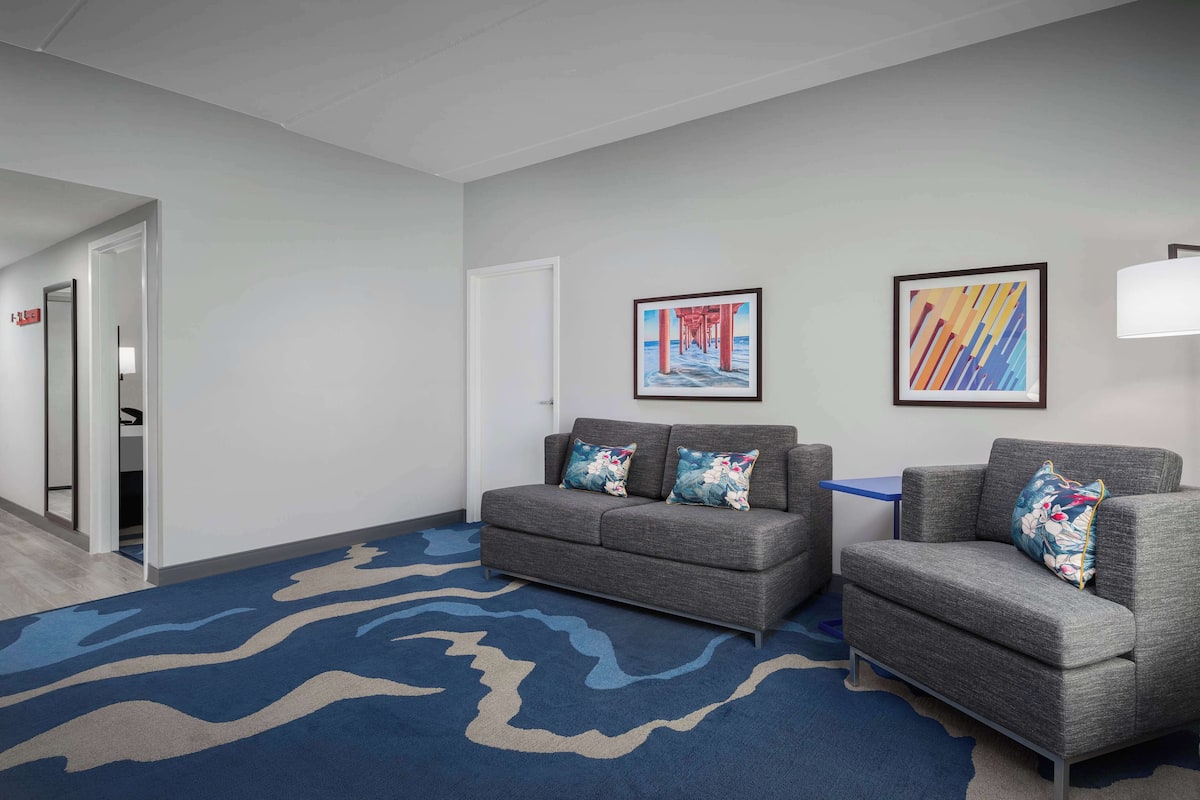 Un hall de hotel con un sofá gris, una alfombra azul y dos obras de arte enmarcadas en la pared.