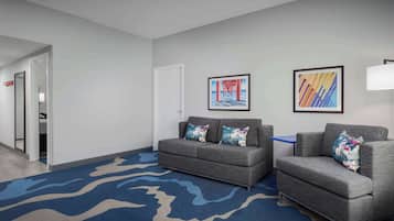 A hotel lobby with a grey sofa, a blue rug, and two framed artworks on the wall.