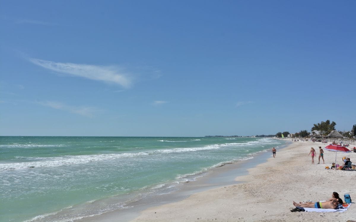 A beach with clear skies, calm waters, and people sunbathing.
