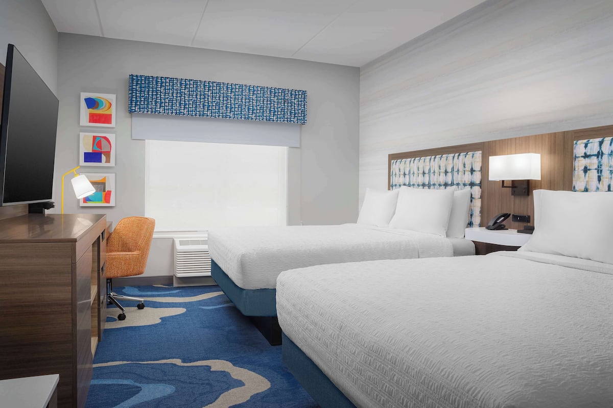 Una habitación de hotel con dos camas, un escritorio, un televisor y una ventana.