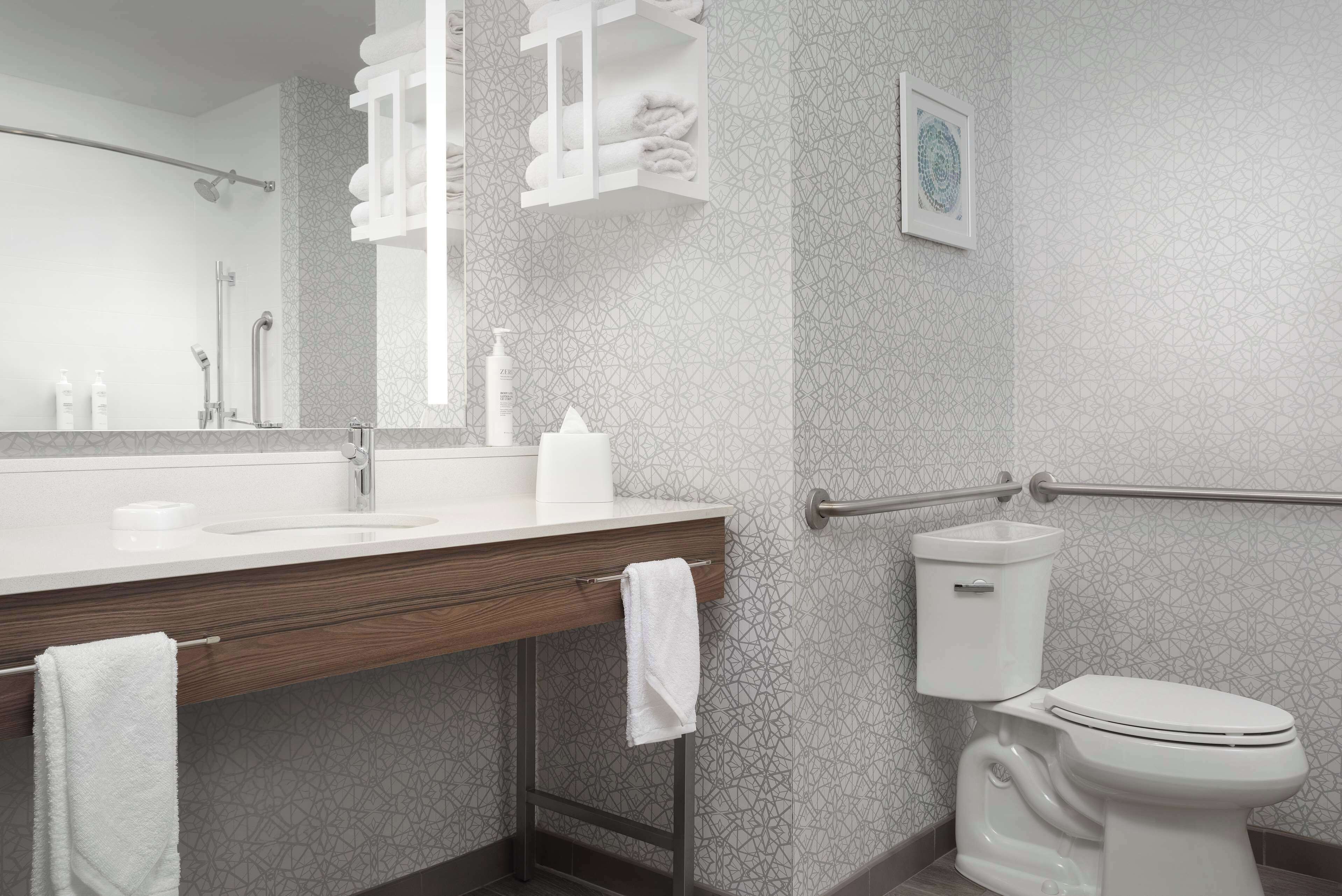 Un baño moderno con un espejo grande, un tocador de madera, un inodoro y un perchero para toallas.