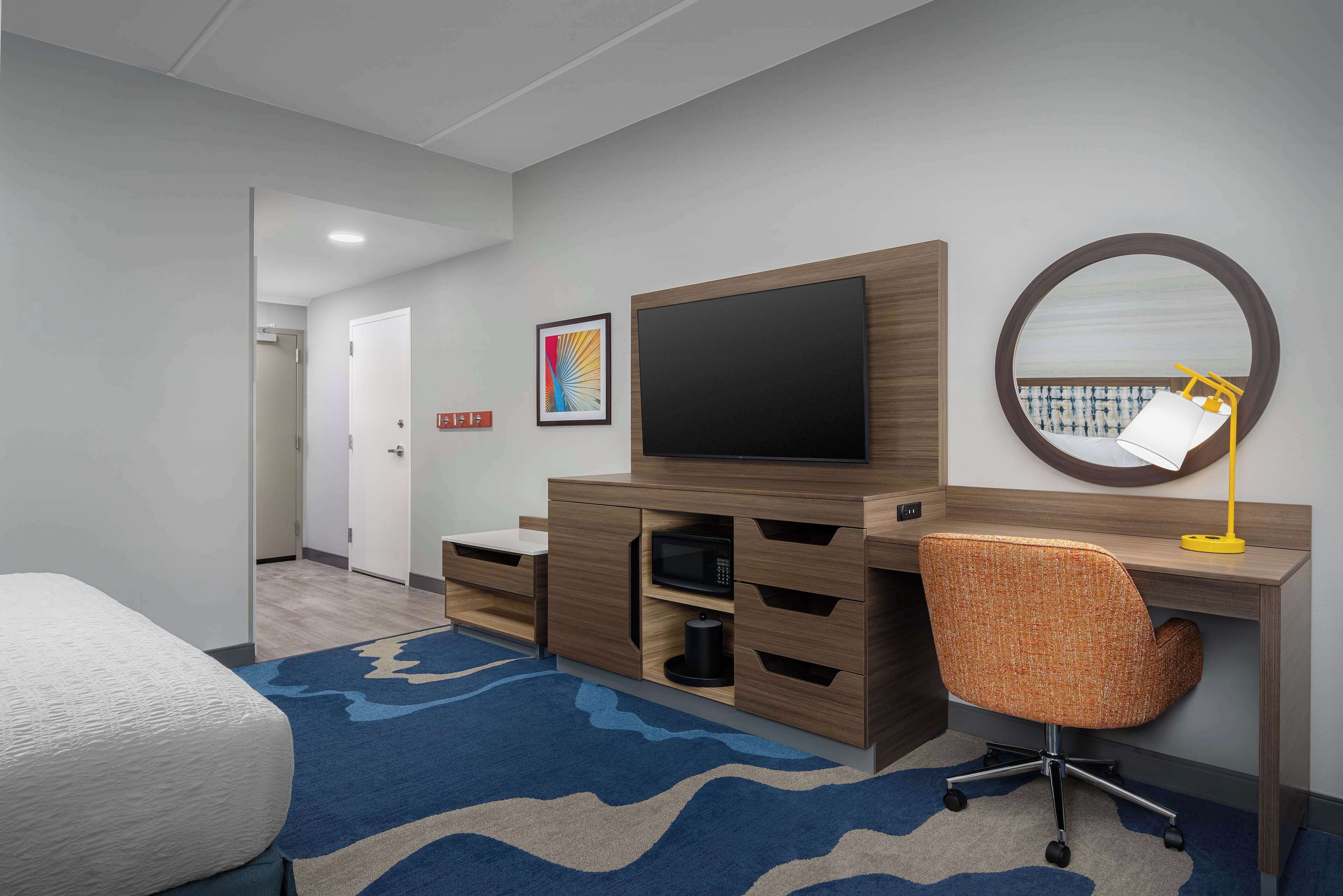 A hotel room with a bed, a desk with a chair, a television, a microwave, and a mirror.
