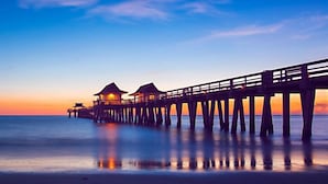 A pier extending into the water with two structures at the end, likely accommodations, during sunset. - Hampton Inn & Suites Naples South (Naples)