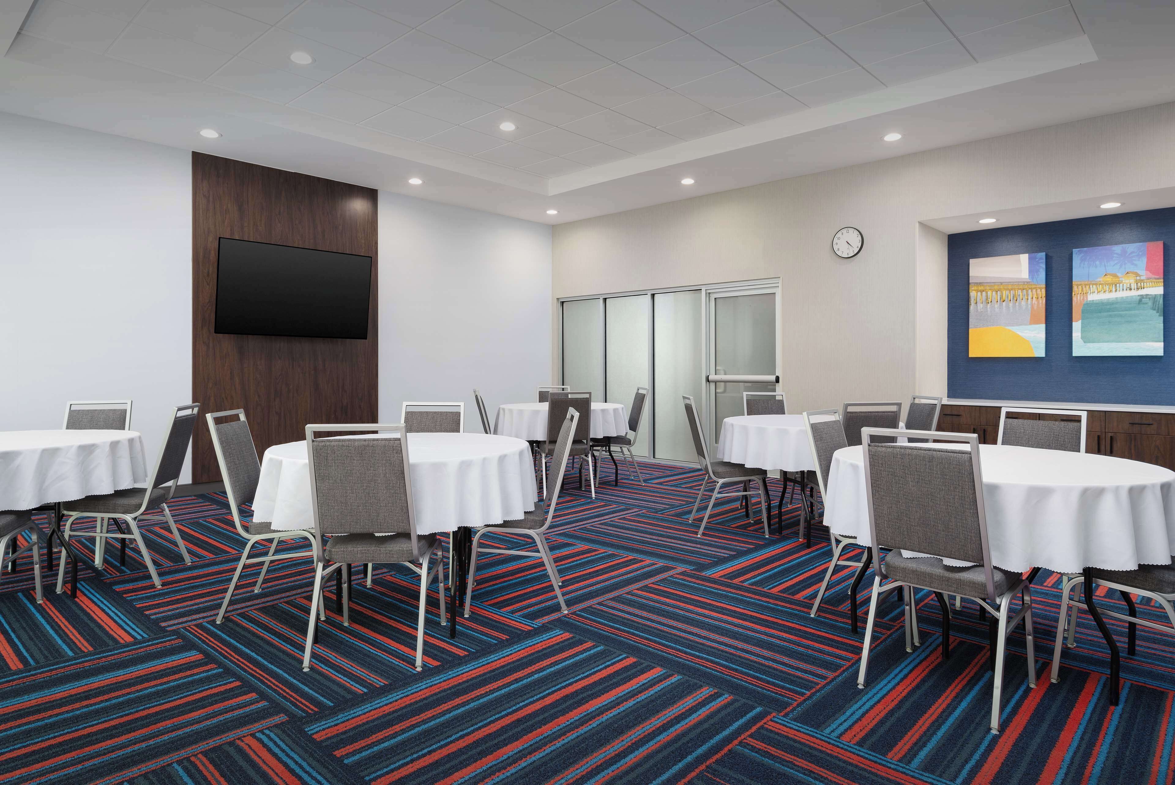 A conference room with round tables and chairs, a flat-screen TV mounted on the wall, and a colorful carpet.