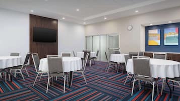 A conference room with round tables and chairs, a flat-screen TV mounted on the wall, and a colorful carpet.