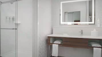 Un baño moderno con cabina de ducha de vidrio, tocador de madera con espejo y un perchero para toallas.