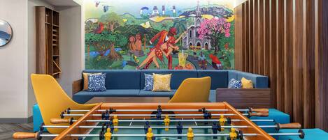Una habitación con mesa de fútbol, un sofá con cojines y un mural colorido en la pared.