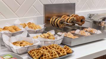 Un bufé con diversas opciones de panadería, como cruasanes, gofres y donas.