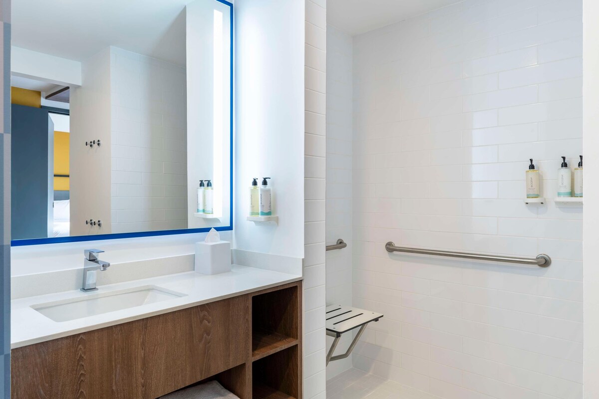 A modern bathroom with a large mirror, two sinks, and a shower area with a grab bar.