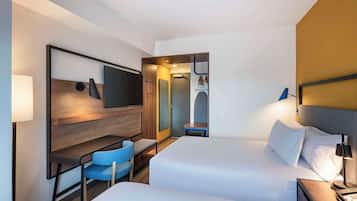 Quarto de hotel com duas camas, uma escrivaninha com cadeira, televisão e espelho.