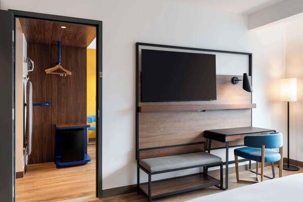 A hotel room with a wooden wardrobe, a flat-screen TV mounted on the wall, a small table with two chairs, and a bedside lamp. - Tru By Hilton Cali Sur (Cali)