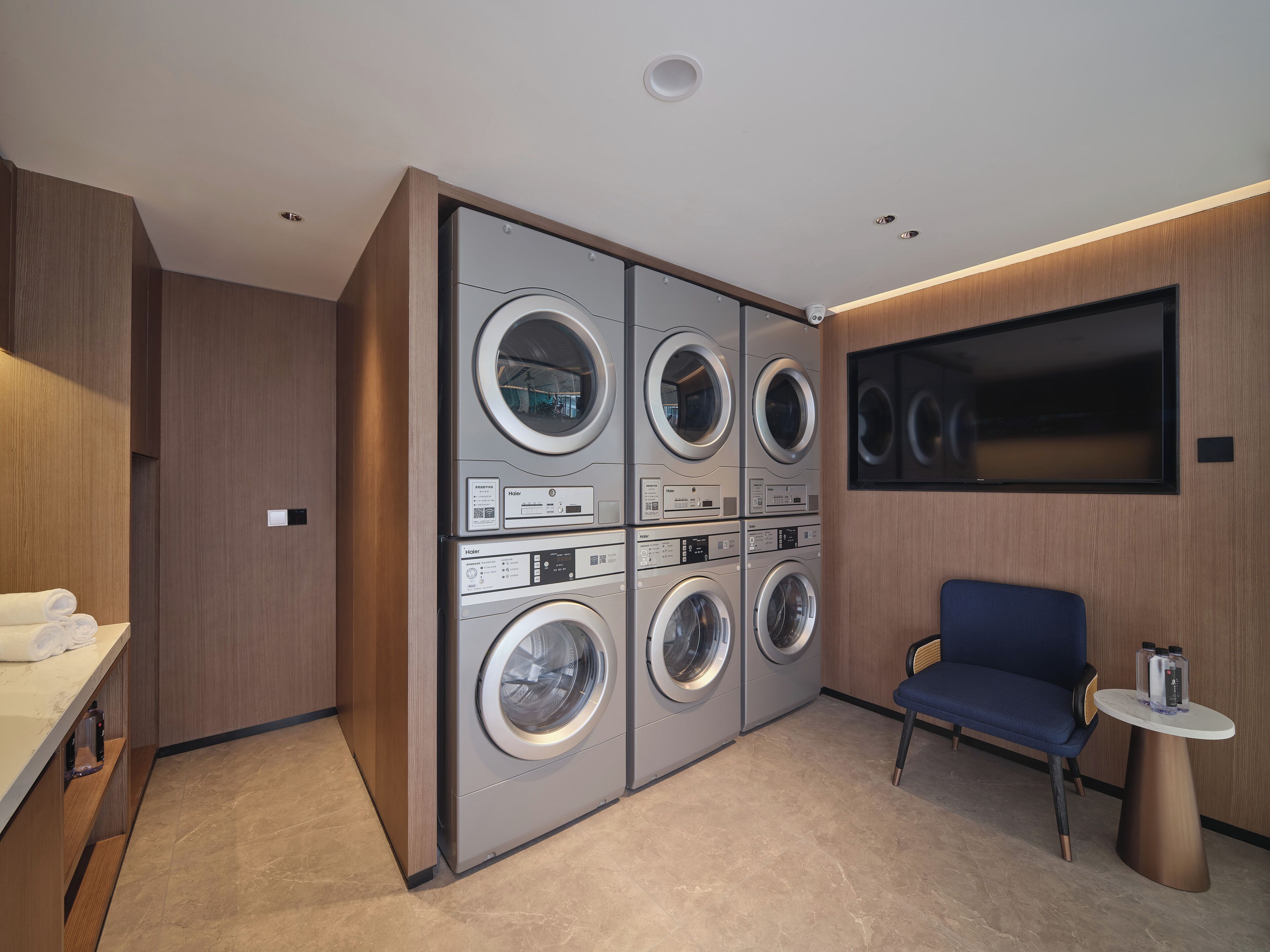 Une buanderie moderne équipée d’un lave-linge et d’un sèche-linge intégrés, d’un coin salon et d’un téléviseur fixé au mur.