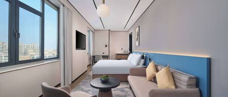 A modern hotel room with a large bed, a sofa, a desk, and a TV.