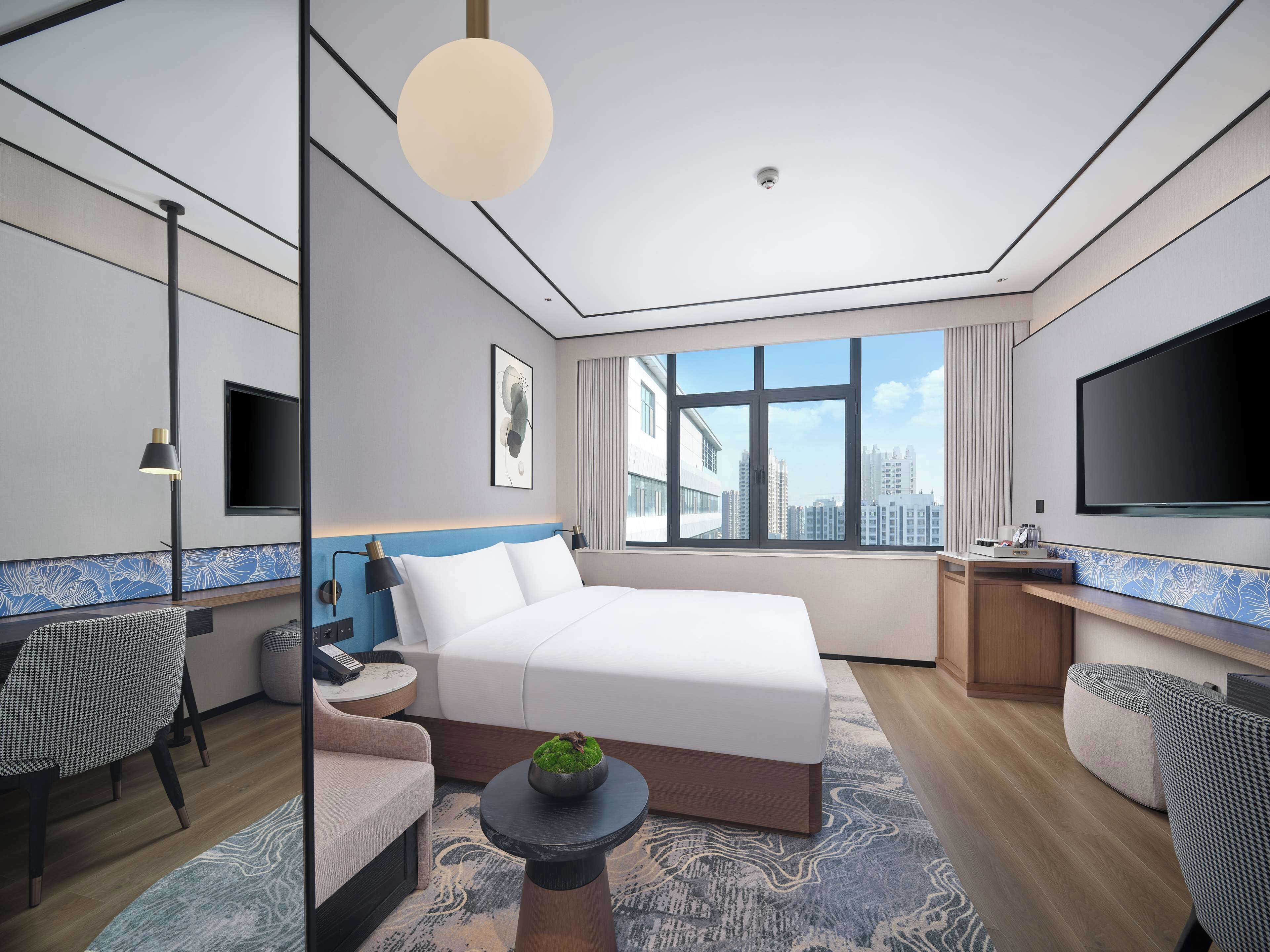 Habitación de hotel moderna con una cama grande, un escritorio, un televisor y vistas a la ciudad.
